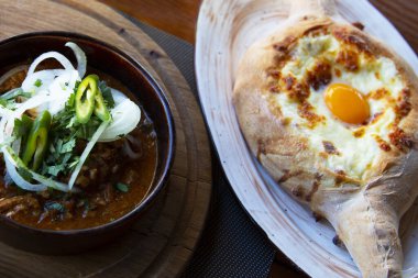 Kafkas mutfağı. Ajarian tarzında Khachapuri fırın ürünleri. Mozzarella ve yumurtalı açık turta. Gürcistan mutfağı, sokak yemekleri, ulusal abur cuburlar. Biftek ve baharatlı Solyanka çorbası. Bardakta bira.