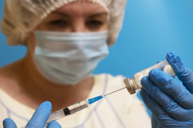 Şırıngayı ilaçla dolduran doktor, yakın çekim. Aşı ve bağışıklık. Maske ve eldiven takan bir kadın doktor ampul ve şırınga ile...