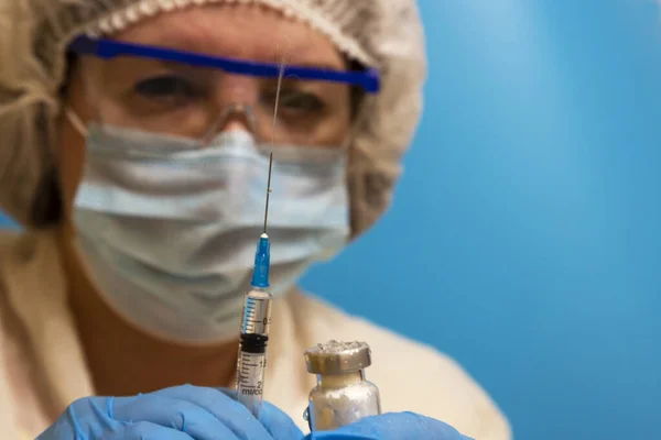 Doctor with a syringe and ampoule, close-up. Vaccination and immunization. A female doctor wearing a mask, protective glasses and gloves with an ampoule and a syringe