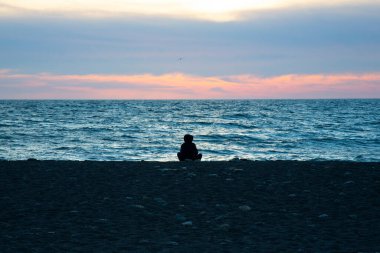 Denizde turuncu gün batımı, günbatımının arka planında bir adamın silueti. Gün batımında bir kız sahilde oturur. Güneş denize battı.