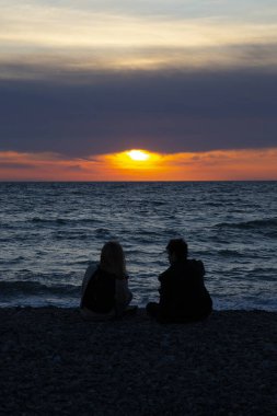 Birbirine aşık çiftler yaz tatilinde sahilde gün batımını izliyorlar. İnsanlar arkada oturup tropikal bir tatil için güneşin batışının tadını çıkarıyorlar. Sahilde romantik bir çift