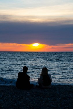 Birbirine aşık çiftler yaz tatilinde sahilde gün batımını izliyorlar. İnsanlar arkada oturup tropikal bir tatil için güneşin batışının tadını çıkarıyorlar. Sahilde romantik bir çift