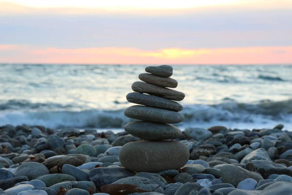 the concept of balance and harmony. stones on the beach in nature. Pyramid of stones on a beach of pebbles, in the background a blurred background of the sea, dawn