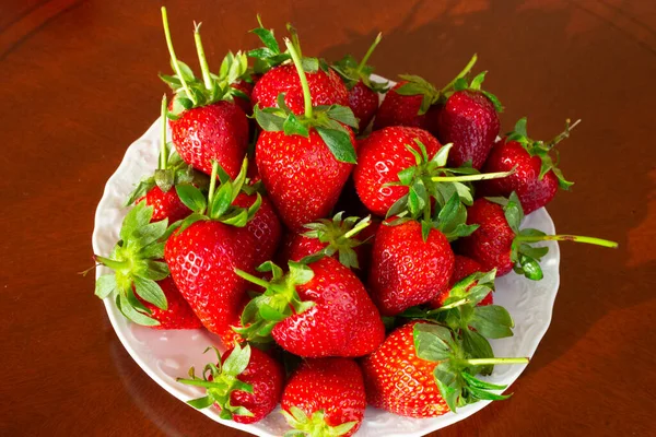 Ώριμες κόκκινες φράουλες σε λευκό πιάτο σε ξύλινο τραπέζι, καλοκαίρι, Ιούλιο — Φωτογραφία Αρχείου