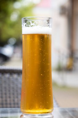 Açık bir kafedeki terasta, tahta bir masanın üzerinde cam bardakla bira. Arkada bir araba var. Yaz tatili