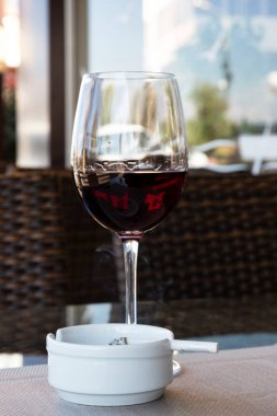 Bir bardakta kırmızı şarap ve sigara beyaz bir kül tablasında bir sokak kafeteryasında, yazın bir restoranın verandasında, kötü alışkanlıklar, alkolizm ve tütün.