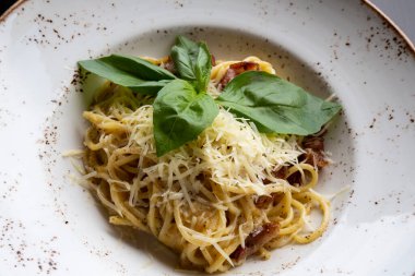 Restoranda masanın üstünde beyaz bir tabakta spagetti carbonara. Pastırma, peynir ve krem soslu Durum buğdayı. Yakın plan.