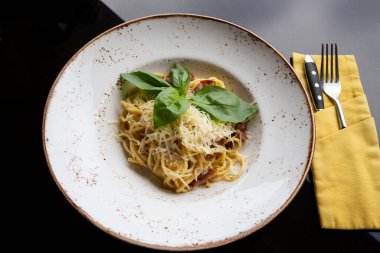 Restoranda masanın üstünde beyaz bir tabakta spagetti carbonara. Pastırma, peynir ve krem soslu Durum buğdayı. Yakın plan.