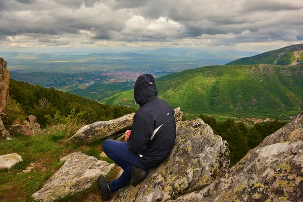 Ein junger reisender mann sitzt auf dem gipfel des berges im prespa nationalpark und genießt die schönheit der landschaft in der nähe der stadt bitola. — Stockfoto