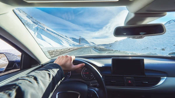 Snowy mountains road view from the modern luxury car interior with drivers hand on steering wheel with gps navigation mockup — 스톡 사진