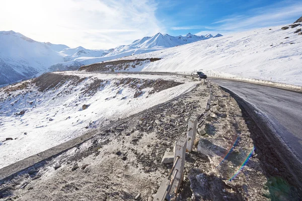Beautiful sunny road twist with car with snowy mountains in background — Stock Fotó