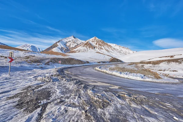Beautiful sunny road twist in the snowy mountains — Stok fotoğraf