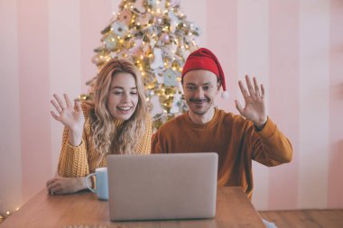 Bilgisayarla video görüşmesi yapan mutlu genç çift, ailelerini Noel ya da yeni yıl tatili ile selamlıyor..