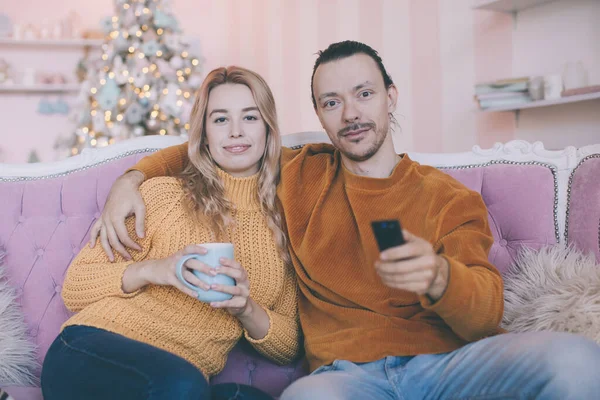 Portrait of a funny couple watching tv sitting on a couch in the living room at home in winter — Stock Photo, Image