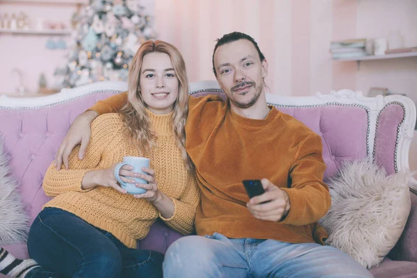 Portrait of a funny couple watching tv sitting on a couch in the living room at home in winter — Stock Photo, Image