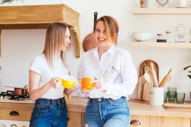 Mutfakta sıcak bir içki içip sohbet eden iki güzel genç kadın.