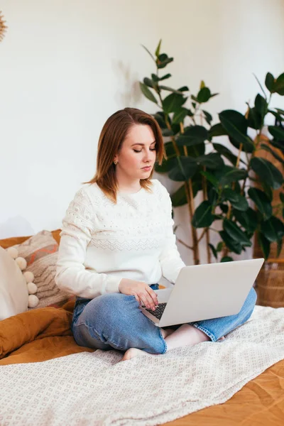 Pretty smiling woman has pleasant smile, haircut, dressed in casual domestic clothes, laugh during watching comedy, leaves comments chats online with friends on laptop computer sits in bed. — Stock Photo, Image