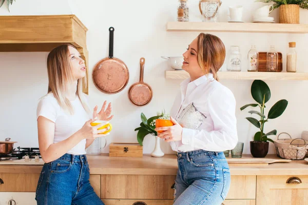 Két gyönyörű fiatal nő beszélget egy meleg ital mellett a konyhában. — Stock Fotó