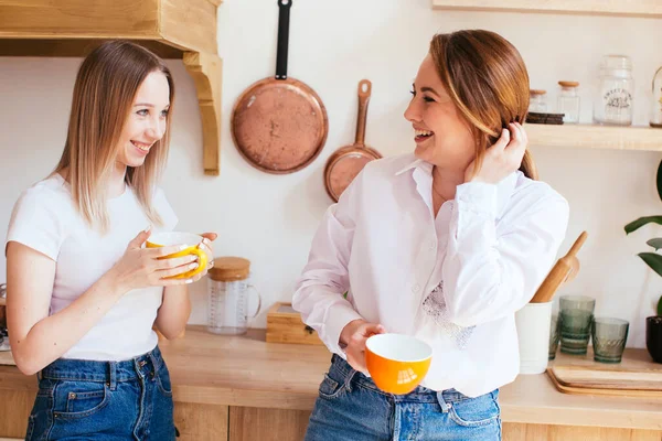 Duas belas mulheres jovens conversando sobre uma bebida quente na cozinha Fotografia De Stock