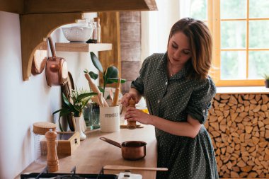 Mutfakta sobanın yanında duran genç bir kadın. Yemek pişirmek ve çeşnilendirmek