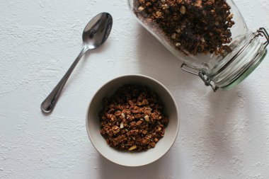 Kahvaltıda çikolatalı granola. Bir kavanoz, bir kase müsli ve bir bardak yoğurt.