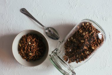 Kahvaltıda çikolatalı granola. Bir kavanoz, bir kase müsli ve bir bardak yoğurt.
