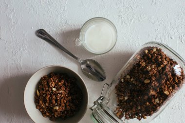 Kahvaltıda çikolatalı granola. Bir kavanoz, bir kase müsli ve bir bardak yoğurt.