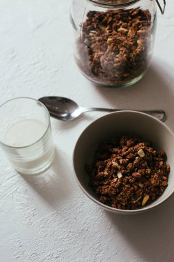 Kahvaltıda çikolatalı granola. Bir kavanoz, bir kase müsli ve bir bardak yoğurt.