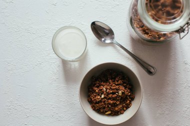 Kahvaltıda çikolatalı granola. Bir kavanoz, bir kase müsli ve bir bardak yoğurt.