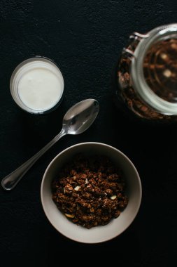 Kahvaltıda çikolatalı granola. Bir kavanoz, bir kase müsli ve bir bardak yoğurt.
