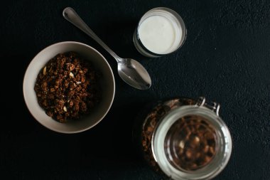 Kahvaltıda çikolatalı granola. Bir kavanoz, bir kase müsli ve bir bardak yoğurt.