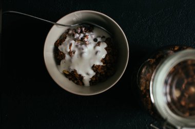 Kahvaltıda çikolatalı granola. Bir kavanoz, bir kase müsli ve bir bardak yoğurt.