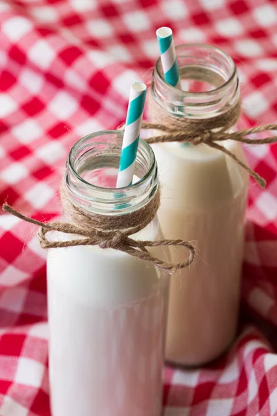 Dos botellas de leche con paja retro azul sobre tela roja —  Fotos de Stock
