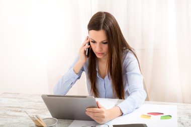 Tablet ile ofiste çalışan ve telefonla konuşuyor