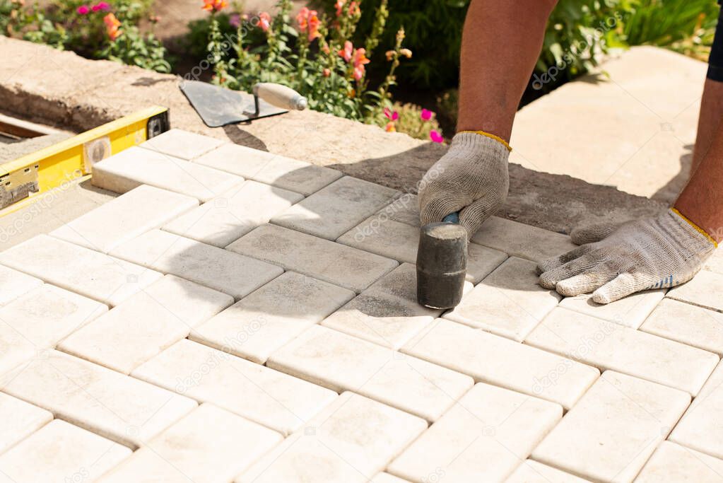 The master lays paving stones in layers. Garden brick pathway paving by professional paver worker. Laying gray concrete paving slabs in house courtyard on sand foundation base.