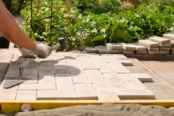 De meester legt tegels in lagen. Tuin bakstenen pad bestrating. Betonnen plavuizen in het huis binnenplaats op zand fundering basis — Stockfoto