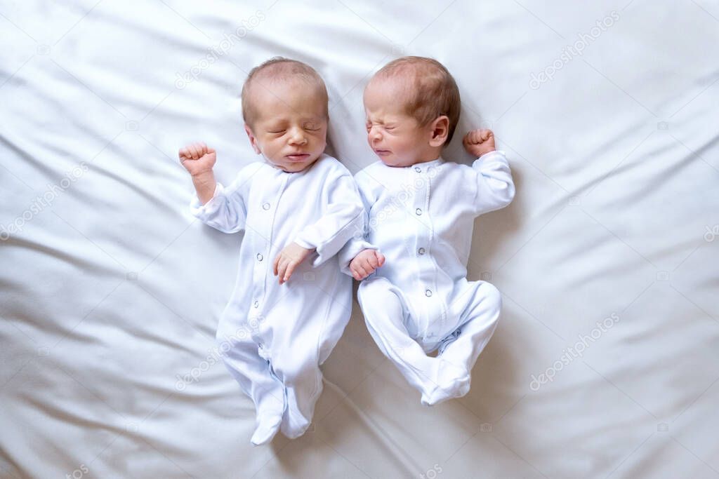 Newborn twins on the bed, in the arms of their parents, on a white background. Life style, emotions of kids. Multiple pregnancy. The large family
