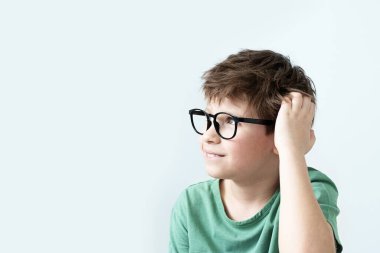 Yeşil tişörtlü ve gözlüklü şaşkın çocuk başını kaşımış. Boşluğu kopyala.