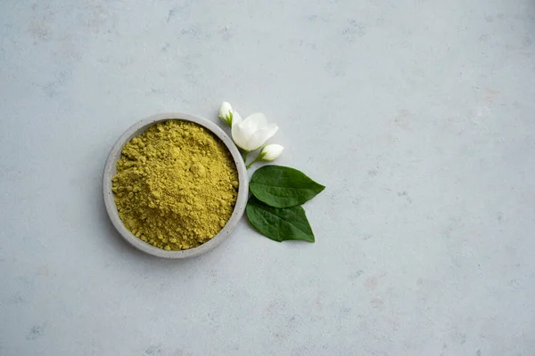 henna powder for dyeing hair and eyebrows and drawing mehendi on hands on a gray cement pedestal with dried flowers or a white flower.