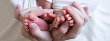 Anne ve babanın elleri yeni doğmuş iki ikiz bebeğinin küçük bacaklarını tutuyor. Döllenme dışı döllenme. çoklu hamilelik