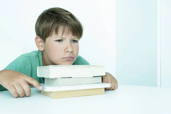 Szomorú fiú könyvvel házi feladatot csinál. Vissza a suliba. Boldogtalan iskolás fiú tankönyvekkel. Távolságtartó tanulás — Stock Fotó