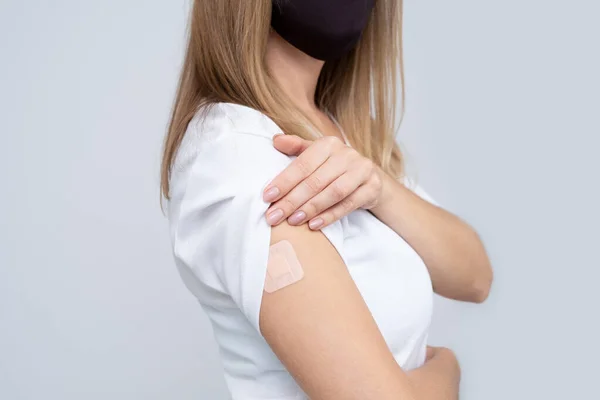 Młoda, piękna, nierozpoznawalna kobieta w masce twarzy, białej koszulce i okularach z gipsem na dłoni cieszy się z otrzymania szczepionki przeciw zakażeniu Covid-19. przestrzeń kopiowania . — Zdjęcie stockowe