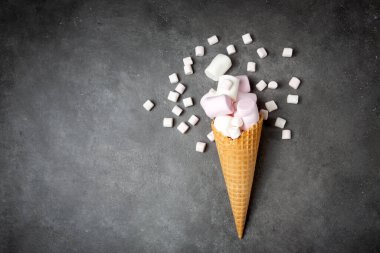 Şekerlemeli gözleme külahı. Koyu gri arka planda pembe, beyaz, narin bir lokum. Favori çocuk şekerleri. Uzayı kopyala, düz yat.