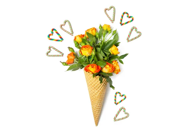 Fresh yellow-orange spray roses in a waffle cone on a white background. Hearts are made from candy canes. Postcard for February 14. Copy space, flat lay.