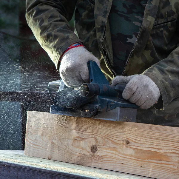 Elektrikli planörü olan bir katılımcının elleri. Uçan talaşlar, ahşap tahta. Bir profesyonelin işi. Ahşap.