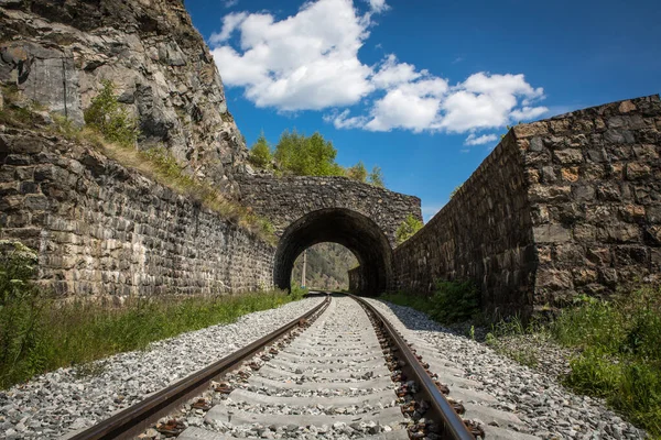 Circum-Baikal Railway. Tunnel and powerful fencing walls. Summer sunny day, blue sky. Railway rails in the foreground.