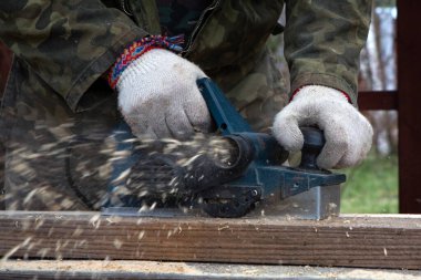 Elektrikli planörü olan bir katılımcının elleri. Uçan talaşlar, ahşap tahta. Bir profesyonelin işi. Ahşap.