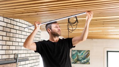 Elektrikçi iş başında. Elektrik kablolarının tamiri ve tavan lambalarının değiştirilmesi için servis. Bir müteahhit çatı katı tarzı ahşap bir tavan kuruyor. Kiralık centilmen ev işlerine yardım ediyor..
