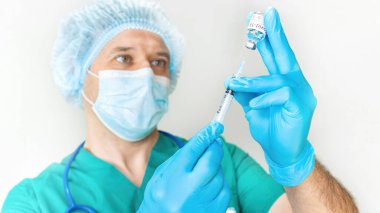 Koruyucu kıyafetli bir doktor COVID-19 aşısı yapmaya hazırlanıyor. Coronavirus aşısı için tıbbi hizmetler. Doktor şırıngayı yakın çekime alıyor..