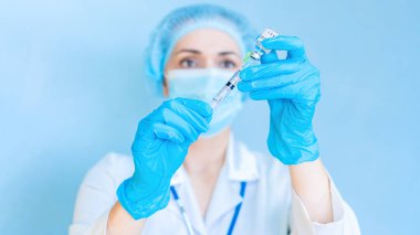 Covid-19 Coronavirus aşısı enjekte etmeye hazırlanan bir doktorun heyecan verici bir fotoğrafı. Doktor şırıngayı ve ilacı göz hizasında tutuyor. Nüfusun planlı aşılanma kavramı.